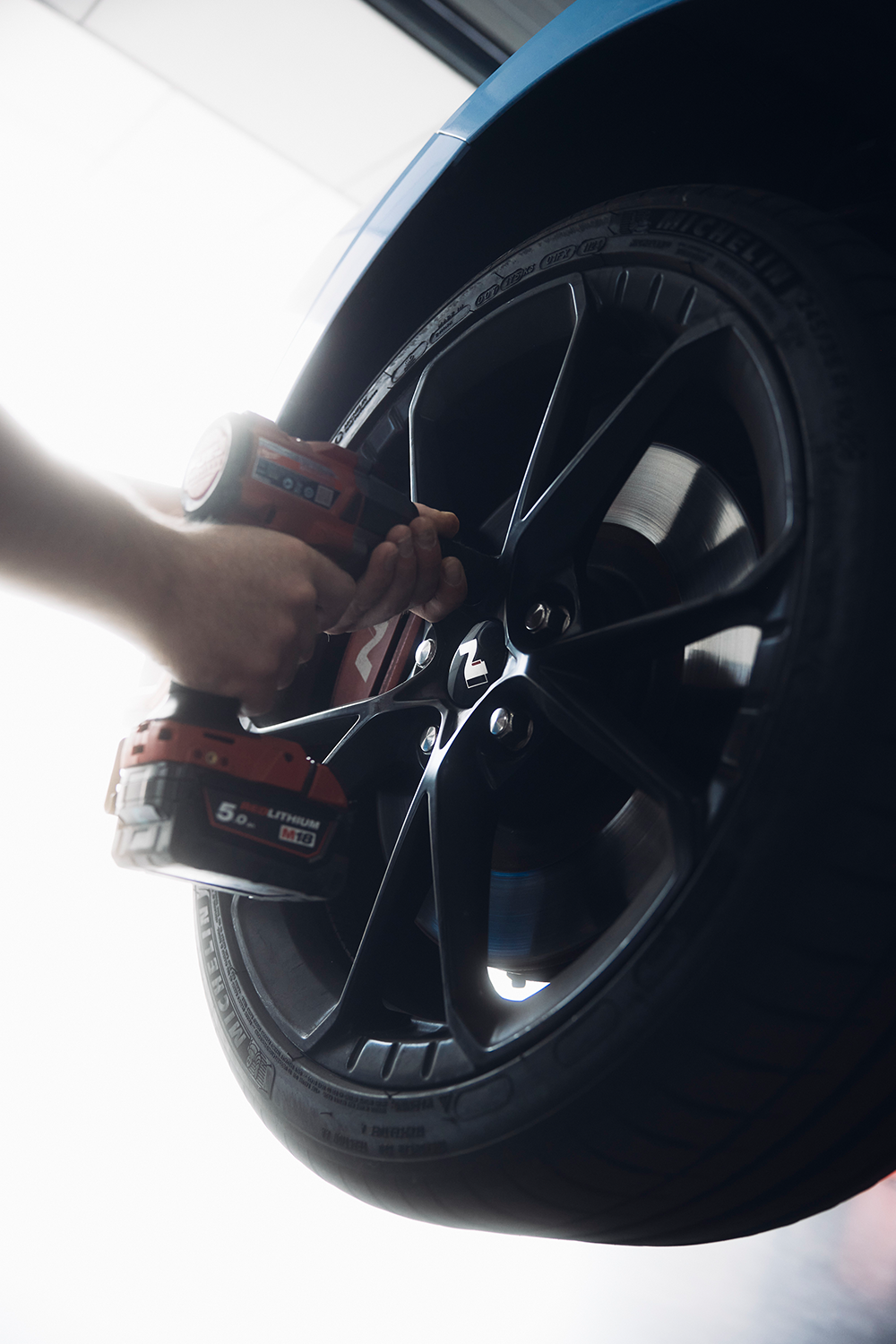 A set of automotive tools on a stainless steel workbench, including a tire pressure gauge, air hose, wrench, pliers, gloves, and a red utility knife.
