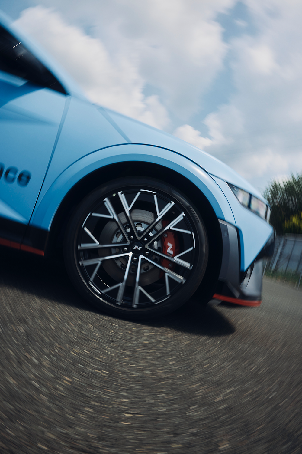 Motion shot of a Hyundai IONIQ 5 N in Performance Blue, focusing on its spinning alloy wheel with red N-branded brake caliper.
