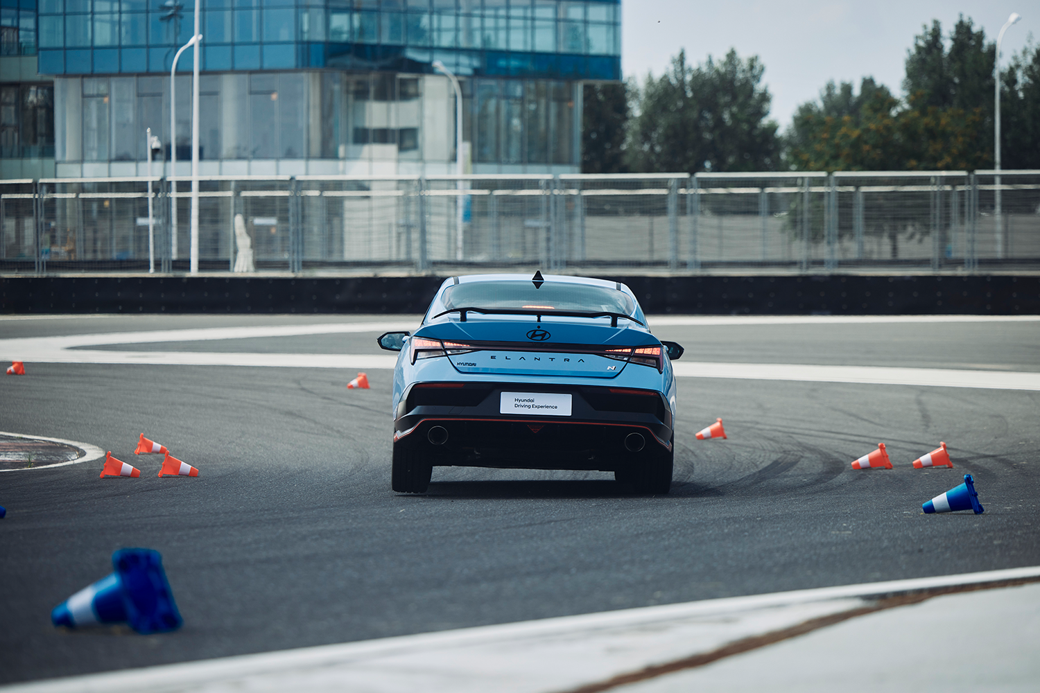 A Hyundai Elantra N in Performance Blue navigating a racetrack, kicking up cones during a Hyundai Driving Experience event.
