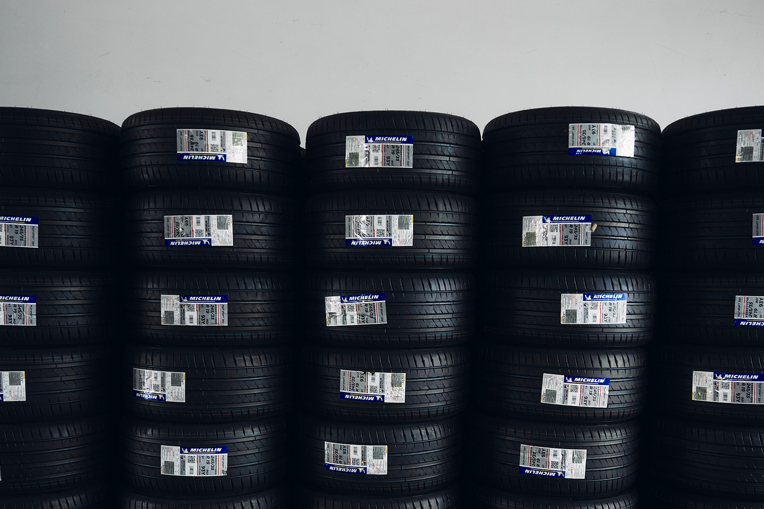 Stacks of new Michelin tires with labels, neatly arranged against a white wall.
