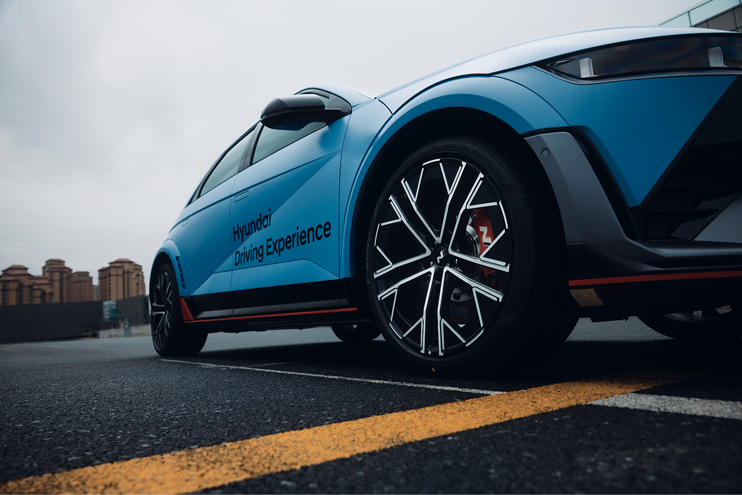 Close-up of a Hyundai IONIQ 5 N at a Hyundai Driving Experience event, highlighting its geometric alloy wheel and red N-branded brake caliper.
