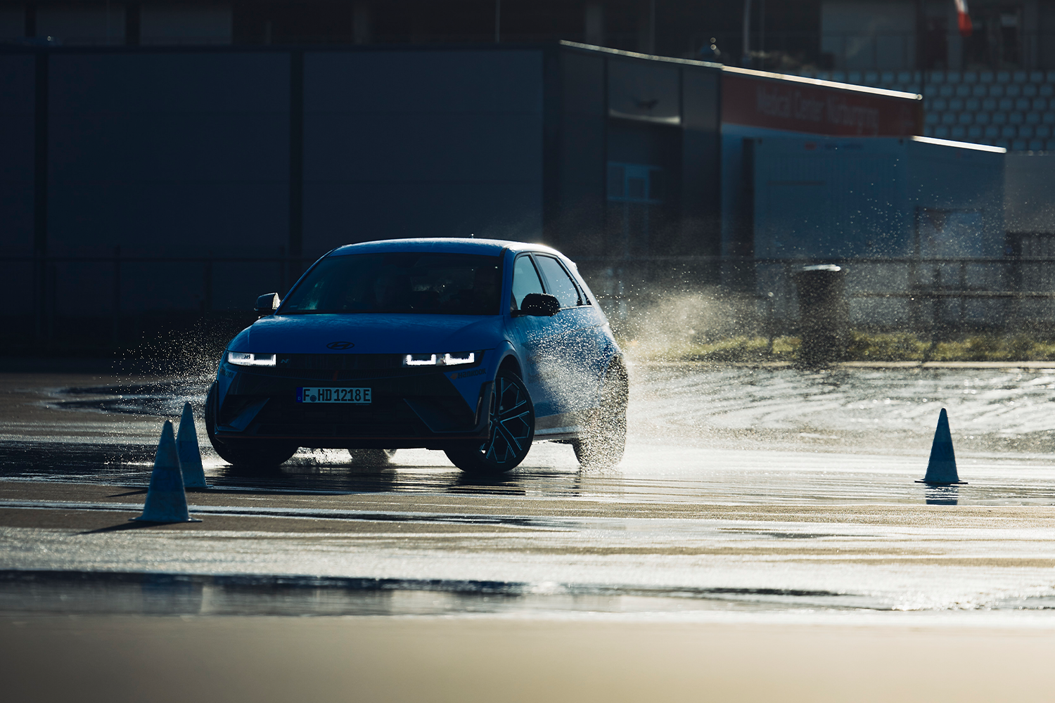 A Hyundai IONIQ 5 N drifts through a wet course, splashing water while navigating between cones during a driving event.
