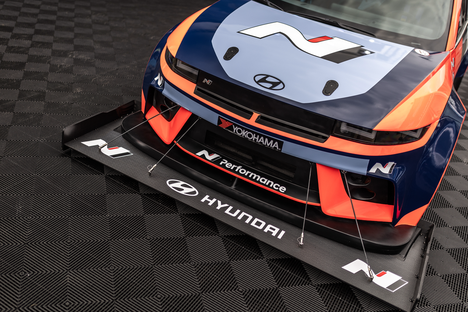 Close-up of the front splitter and hood of the Hyundai N Performance race car, showcasing its aerodynamic components, vibrant livery, and branding from sponsors like Yokohama and Hyundai.
