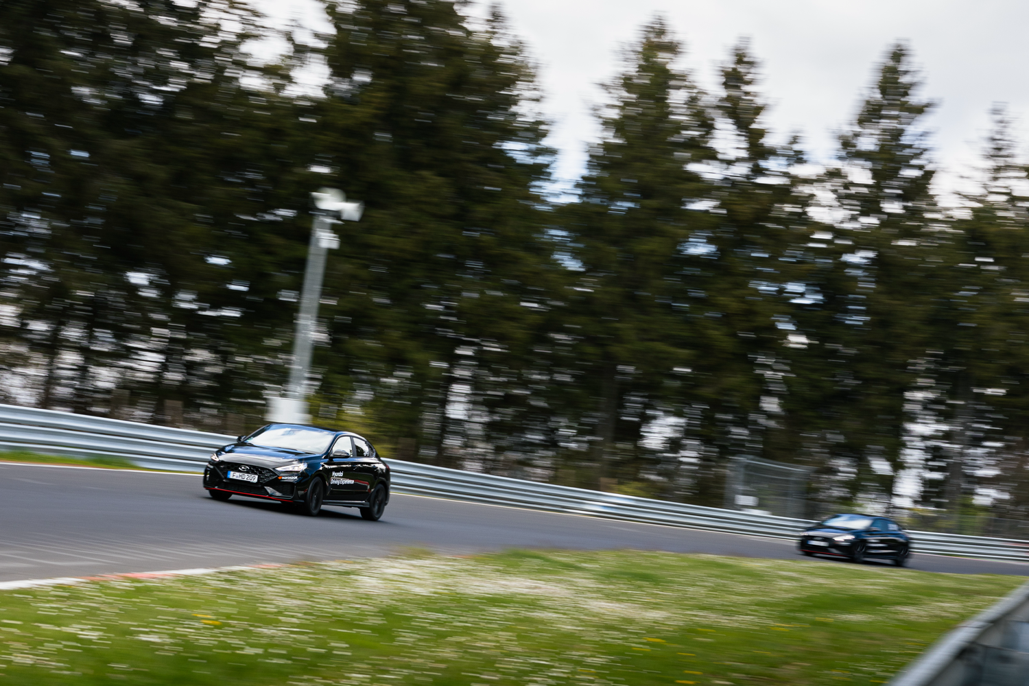 A Hyundai Elantra N in black speeds through a curve on the Nürburgring Nordschleife, with motion blur emphasizing its dynamic performance.
