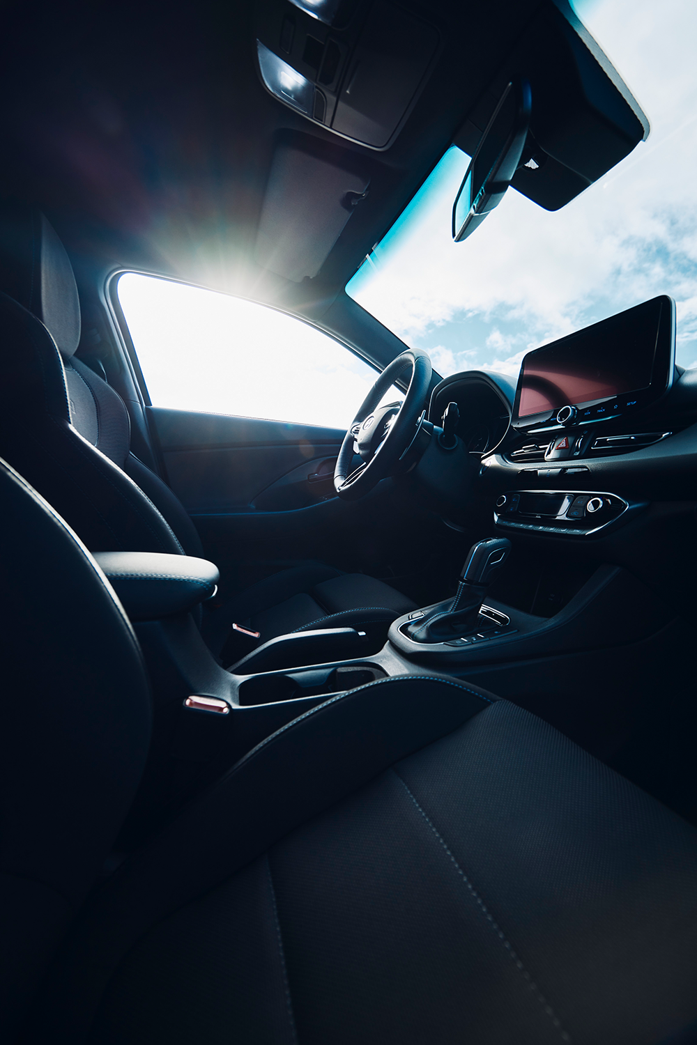 Interior view of the Hyundai IONIQ 5 N from the passenger seat, highlighting the modern cockpit, gear shifter, and dashboard with sunlight streaming through the window.

