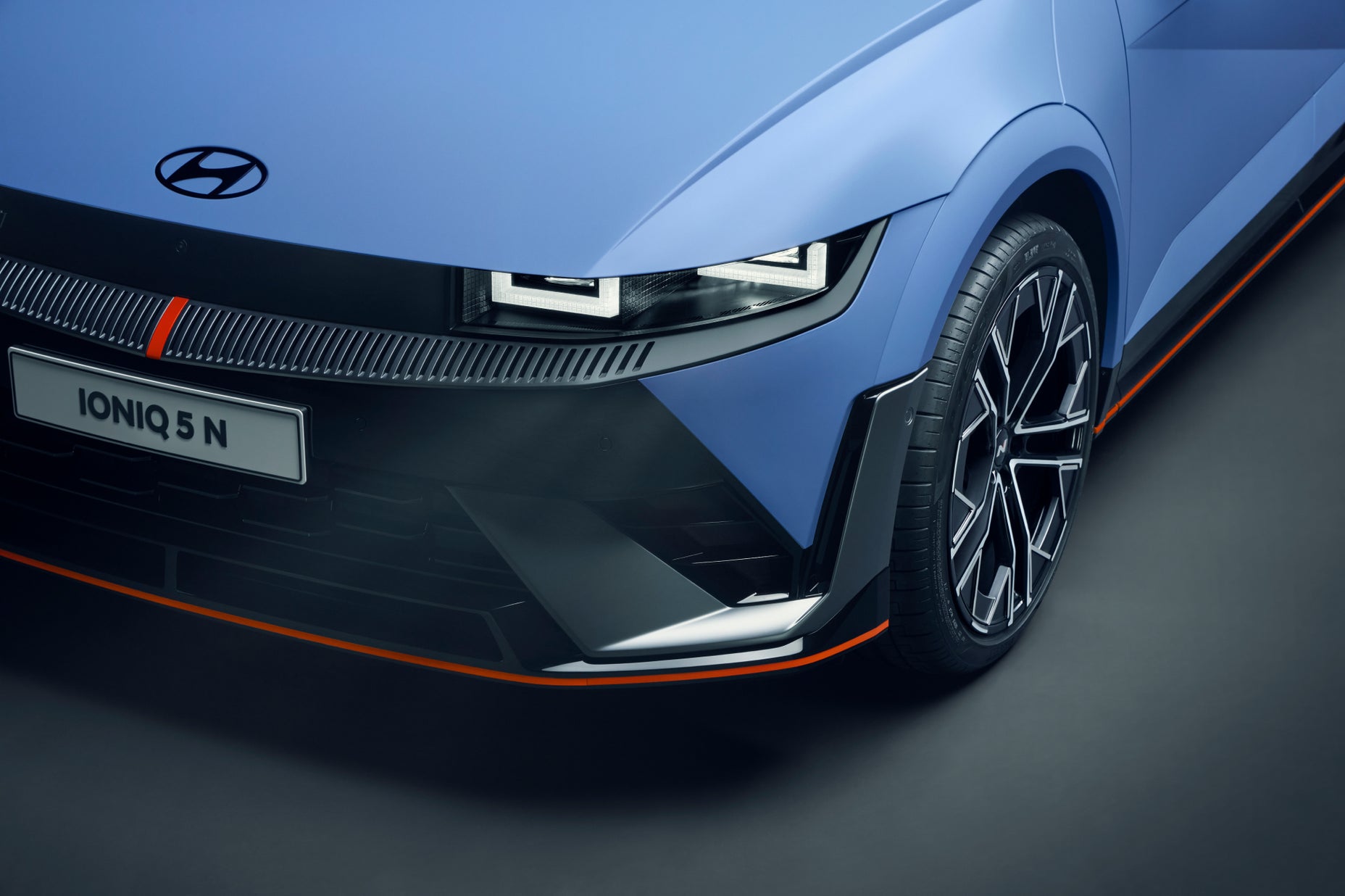 Close-up of the front corner of the Hyundai IONIQ 5 N, showcasing its LED headlights, bold grille, aerodynamic lines, and sporty alloy wheel design.
