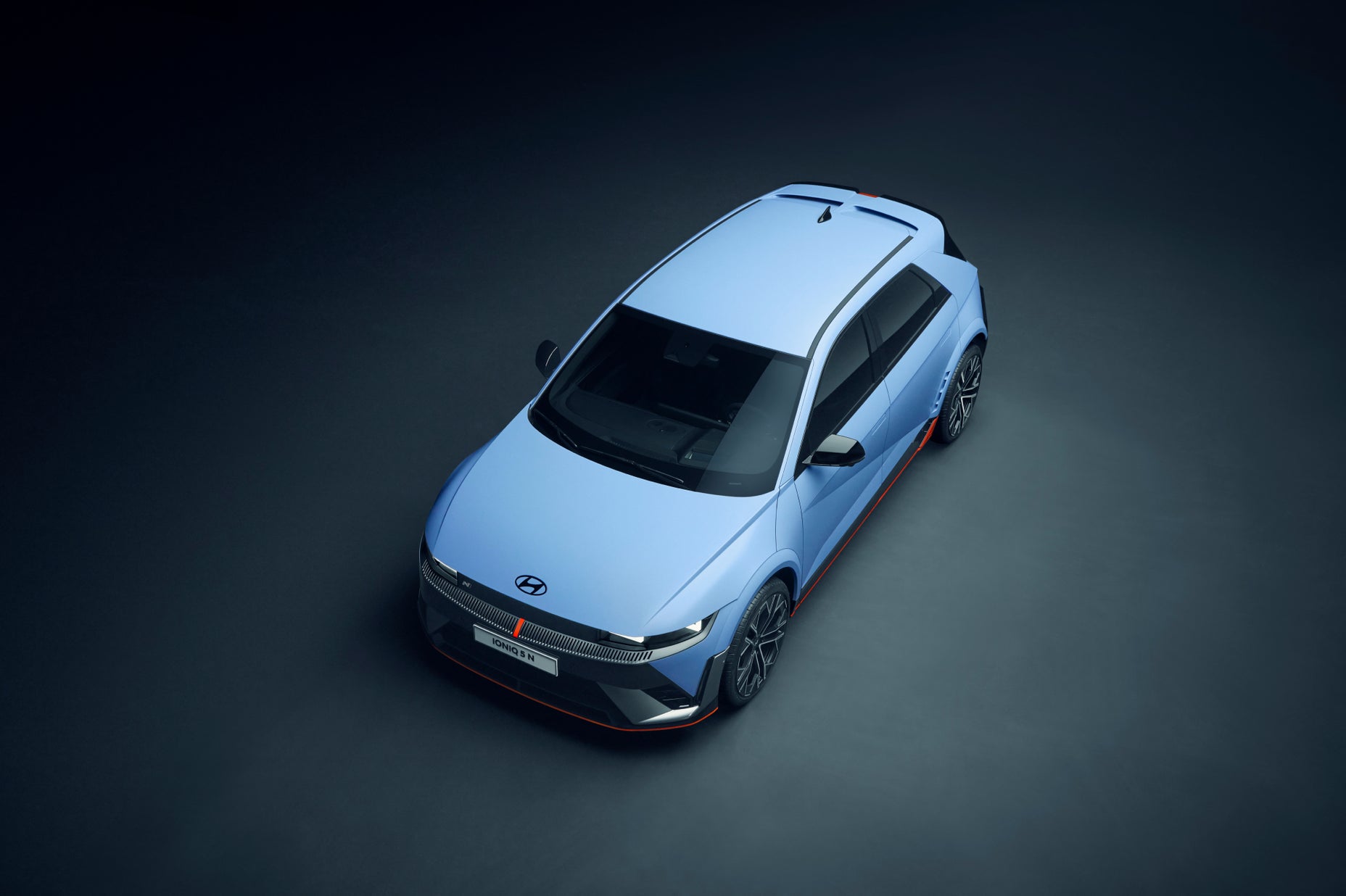Top-down view of the Hyundai IONIQ 5 N under studio lighting, showcasing its aerodynamic design, sharp lines, and sporty roof details against a dark background.
